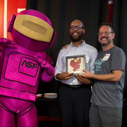 2 men standing with astronaut mascot